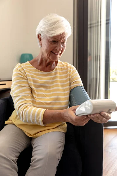 自宅のソファに座って血圧をチェックしている白人のシニア女性の中央部 医療と定年退職シニアライフスタイルの概念 — ストック写真