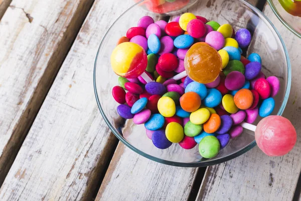 多色棒棒糖和巧克力糖果在木制白桌玻璃碗中的高角度视图 不变的 不健康的饮食和甜食概念 — 图库照片
