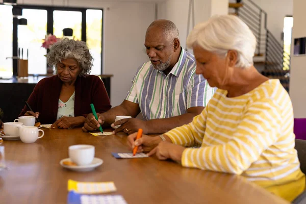 Multiraciale Senior Vrienden Met Koffiekopjes Eettafel Spelen Bingo Verpleeghuis Geluk — Stockfoto