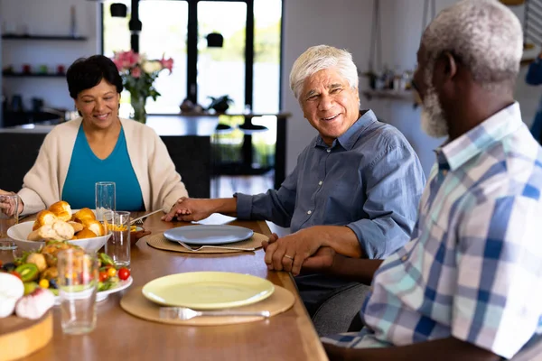 在养老院 多种族微笑的老朋友牵着手 在餐桌边聊天 不变食物 辅助生活和退休 — 图库照片