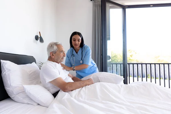 Biracial Female Physiotherapist Assisting Caucasian Senior Man Lying Bed Home — Stock Photo, Image