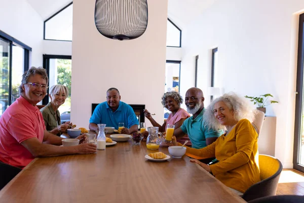 stock image Portrait of smiling multiracial senior friends with breakfast on dining table in retirement home. Unaltered, food, drink, healthy, togetherness, support, assisted living and retirement concept.