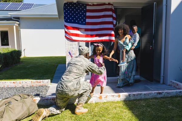 stock image Multiracial family with excited girl running towards military father to embrace him in yard. Happy, unaltered, family, together, childhood, military, patriotism, flag of america, homecoming, pride.