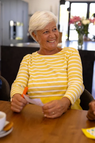 Весела Старша Жінка Тримає Картку Бінго Дивлячись Далеко Сидячи Обіднім — стокове фото