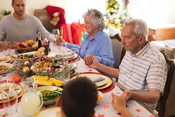 多世代の白人家族がクリスマスディナーのテーブルに一緒に座り 手を祈り 握っています クリスマスに家族で楽しむ生活の質 — ストック写真