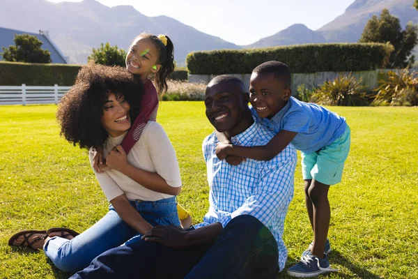 快乐的多种族孩子从后面抱着父母 坐在院子里的草地上 不变的家庭 夏天和自然的概念 — 图库照片