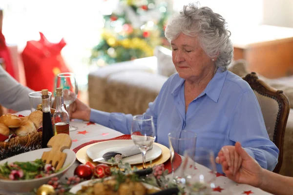 年配の白人女性がテーブルに座り 夕食前に目を閉じて祈ります 質の高いライフスタイルの家族で — ストック写真