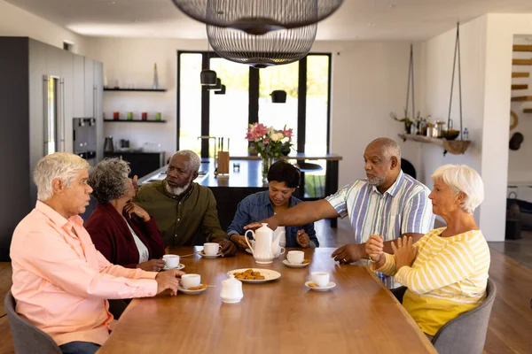 在养老院的餐桌边 多种族的老朋友一边聊天一边享用着饼干咖啡 不变的 辅助生活 — 图库照片