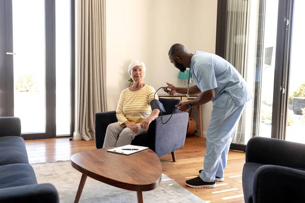 アフリカ系アメリカ人男性医師は 自宅でゲージで白人高齢女性の血圧を調べる アームチェア 変更されていない 高血圧 退職と回復の概念 — ストック写真