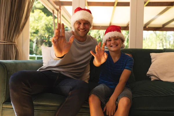 Kafkasyalı Bir Adamla Oğlunun Noel Baba Şapkası Takıp Kanepede Oturup — Stok fotoğraf