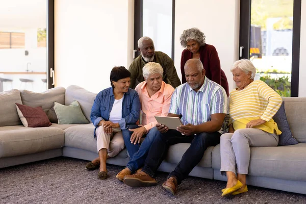 Wielorasowych Seniorów Patrzących Cyfrowe Tablety Pomocą Męskiego Przyjaciela Siedzącego Kanapie — Zdjęcie stockowe