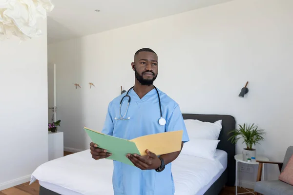 非裔美国男性卫生工作者拿着一个文件站在卧室里在家里 医疗和保健概念 — 图库照片