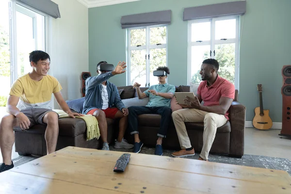 Wielorasowe Męskie Przyjaciele Patrząc Przez Symulatory Rzeczywistości Wirtualnej Siedząc Kanapie — Zdjęcie stockowe