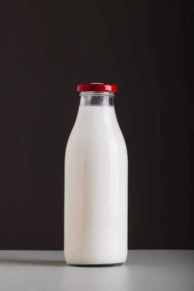 Milk in glass bottle on table against black background with copy space. unaltered, food, drink, studio shot and healthy food concept.