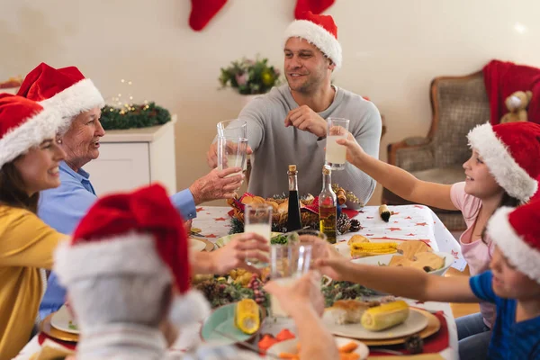 一代又一代的高加索人家庭一起坐在餐桌前吃饭 戴着桑塔帽 面带微笑 优质家庭时间圣诞庆祝活动 — 图库照片