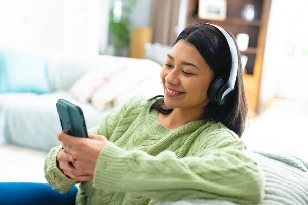 照片中快乐的女人坐在家里的沙发上用智能手机耳机 复制的空间 技术和家庭生活概念 — 图库照片