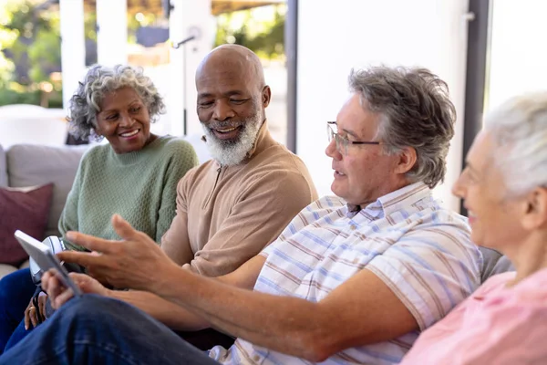 白种人老人与多种族朋友坐在疗养院的沙发上 一边用数字键盘 无线技术 辅助生活和退休 — 图库照片