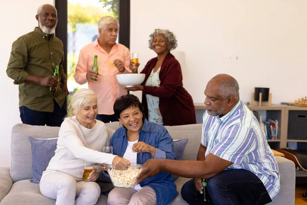 多种族的老朋友在疗养院观看足球比赛时 一边喝啤酒一边吃爆米花 辅助生活和退休 — 图库照片