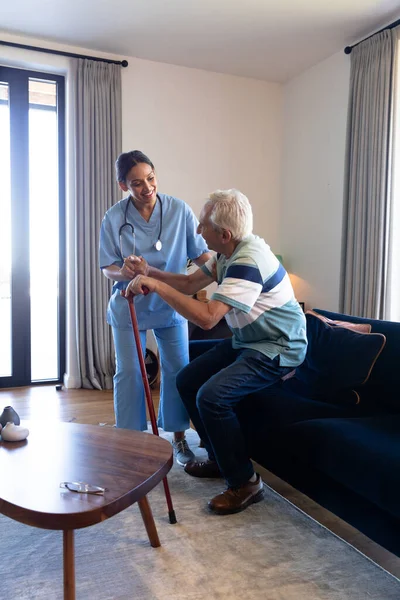 产后女性理疗师帮助高加索老年人在家里从沙发上站起来 医疗保健 — 图库照片