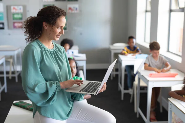 Jovem Professora Branca Usando Laptop Enquanto Senta Mesa Com Estudantes — Fotografia de Stock