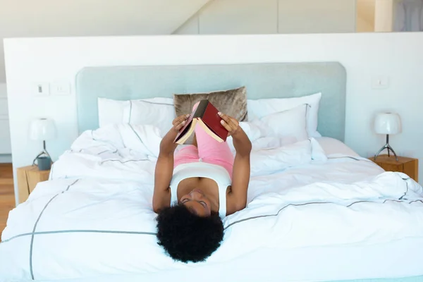 Joven Afroamericana Leyendo Libro Tirado Cama Casa Concepto Relajación —  Fotos de Stock