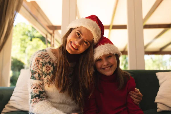 描绘了一个高加索女人和她的女儿呆在家里 戴着桑塔帽 坐在沙发上 看着相机 面带微笑的形象 在圣诞节的时候 我们一起度过了一段美好的时光 — 图库照片