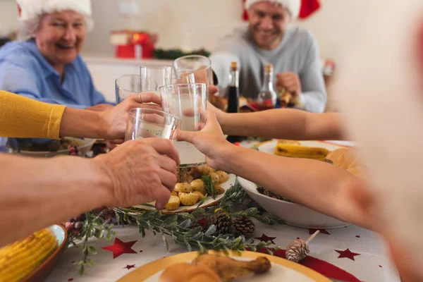 複数世代の白人の家族が一緒に夕食のためにテーブルに座って サンタの帽子をかぶって トーストを作って笑顔になりました 家族の時間クリスマスのお祝い — ストック写真