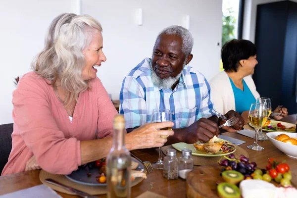 Amigos Seniores Multirraciais Felizes Conversando Enquanto Almoçam Mesa Jantar Lar — Fotografia de Stock