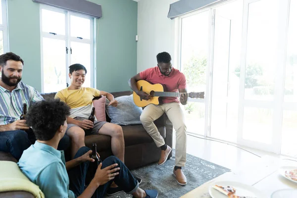 男人一边在家里玩吉他 一边和多种族的朋友聊天和喝啤酒 复制空间 不变的 在一起 社交聚会 周末活动 — 图库照片