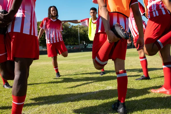Atletas Multirraciais Masculinos Uniformes Vermelhos Esticando Pernas Durante Exercício Playground — Fotografia de Stock