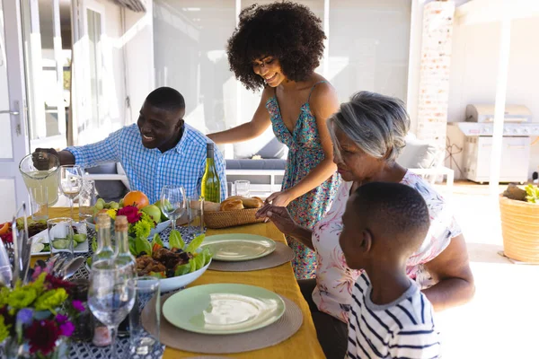 快乐的多种族女人 拥有一头非洲裔头发 在饭桌上为多代家庭提供面包 生活方式和退休观念 — 图库照片