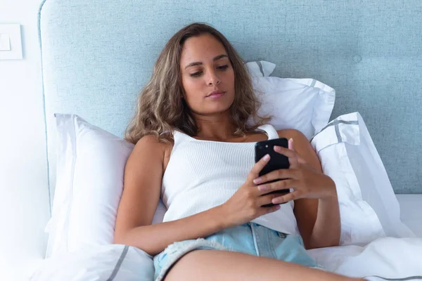 自宅のベッドに横たわっスマートフォンを使用して白人の若い女性 セルフケアとリラクゼーションのコンセプト — ストック写真