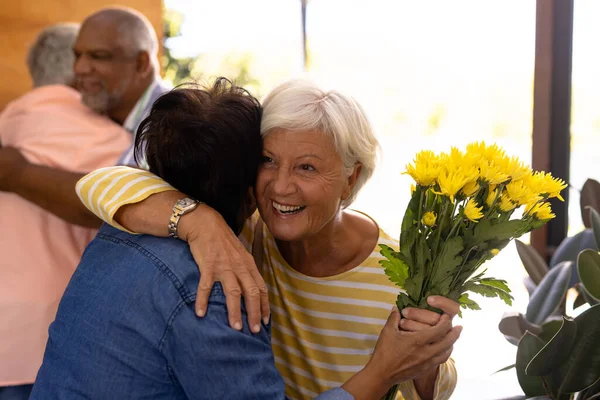 在养老院门口 一群喜形于色的老客人 捧着花束拥抱着朋友 辅助生活和退休概念 — 图库照片