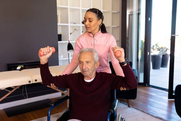 先天性女性理学療法士は 車椅子にダンベルを持ち上げる白人高齢者を支援しています ホーム 変更されていない 理学療法 — ストック写真