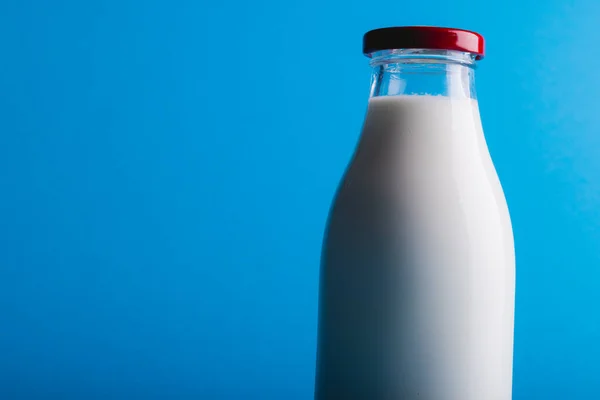 Close-up of milk in glass bottle against blue background with copy space. unaltered, food, drink, studio shot and healthy food concept.