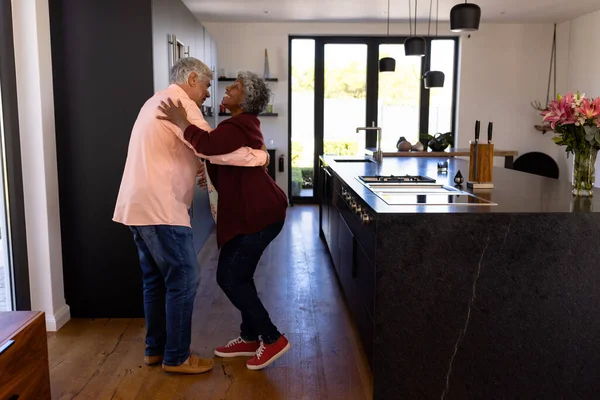 stock image Side view of happy romantic multiracial senior couple dancing in kitchen at retirement home. Unaltered, love, togetherness, enjoyment, support, assisted living and retirement concept.