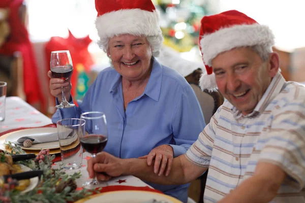 Oudere Blanke Echtpaar Zit Aan Tafel Drinkt Wijn Draagt Kerstmutsen — Stockfoto