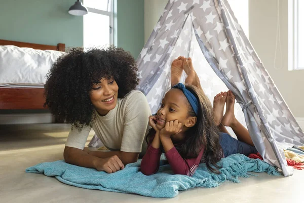 自宅の毛布のテントの中で寝そべっている間 娘と話しているアフロの髪を持つ出産の母親を笑顔 キャンプ 変更されていない 子供時代 ライフスタイルと家庭の概念 — ストック写真