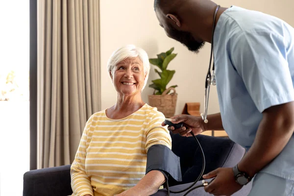 アフリカ系アメリカ人男性の健康労働者は 自宅で白人のシニア女性の血圧をチェックします 医療と定年退職シニアライフスタイルの概念 — ストック写真