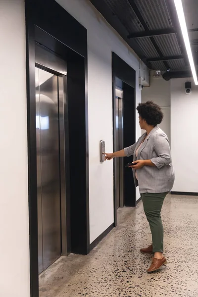 办公大楼中中年女商人按下电梯按钮的侧视图 未经改动的 工作场所 — 图库照片