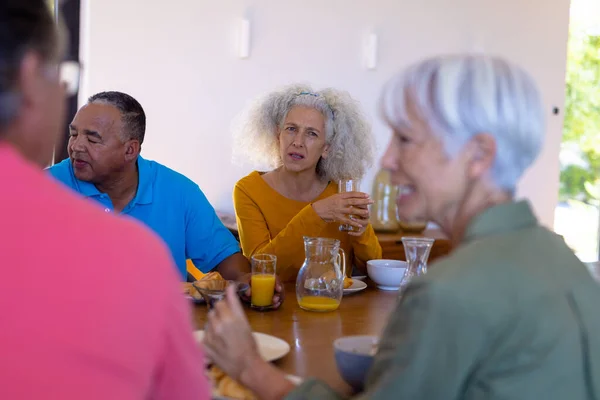 白人老年妇女拿着果汁看着多种族朋友在餐桌边聊天 疗养院 未经改动 辅助生活 退休概念 — 图库照片
