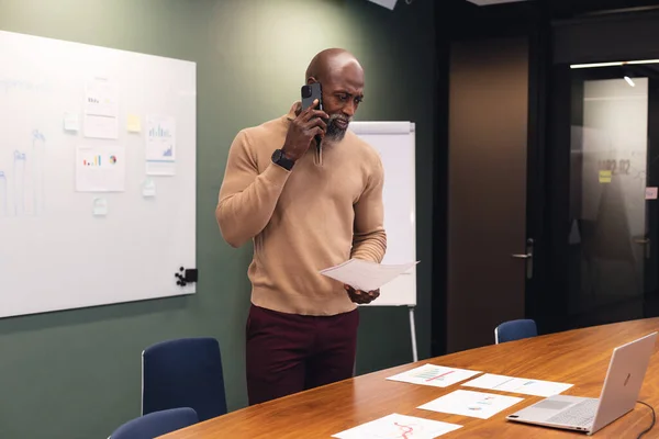 Afrykański Dojrzały Biznesmen Analizuje Dokumenty Rozmawiając Przez Telefon Komórkowy Biurze — Zdjęcie stockowe