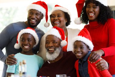 Multi generation african american family posing, smiling and wearing santa hats. quality family time christmas celebration. clipart