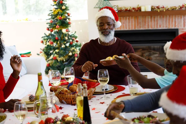 ダイニングルームでの複数世代のアフリカ系アメリカ人の家族は サンタの帽子をかぶって 家族の時間クリスマスのお祝い — ストック写真