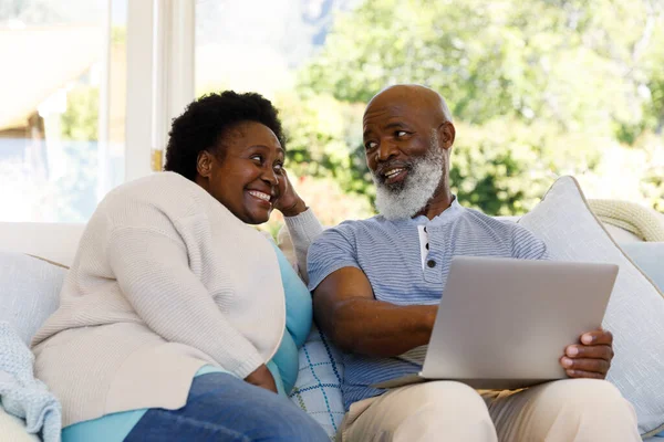 シニアアフリカ系アメリカ人のカップルが一緒に家で時間を過ごします ソファに座って ラップトップコンピュータを使用して笑顔 コロナウイルスCovid 19隔離ロックダウン中に隔離 — ストック写真