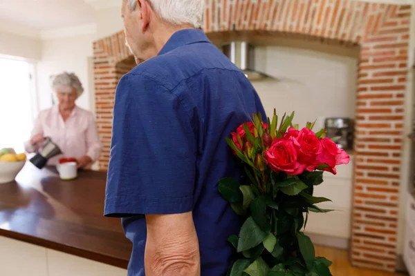 先輩の白人夫婦は一緒に家で時間を過ごし 男は彼の妻にそれらを与える前に 背中の後ろに花の花束を持っていました コロナウイルスCovid 19隔離ロックダウン中に隔離 — ストック写真