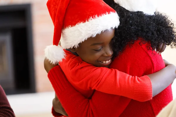 アフリカ系アメリカ人の少年は 彼の母親を受け入れ 笑顔とサンタの帽子を着用 家族の時間クリスマスのお祝い — ストック写真
