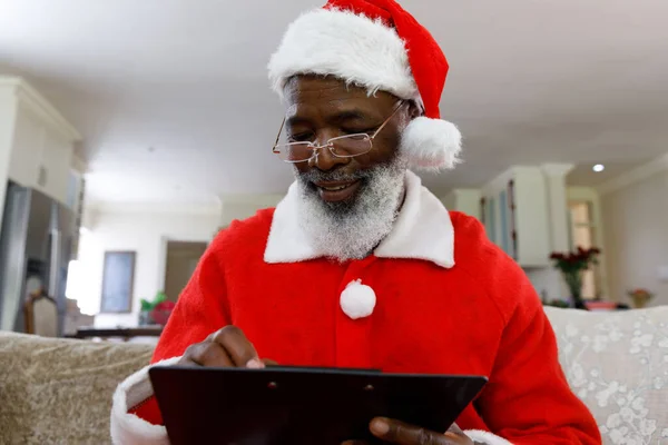 上級アフリカ系アメリカ人の男性はサンタの衣装を着てクリップボードに書き込みます 家族の時間クリスマスのお祝い — ストック写真