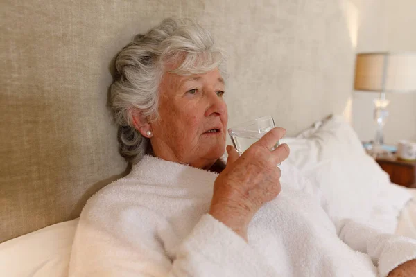 Starsza Biała Kobieta Spędzająca Czas Domu Leżąca Łóżku Trzymająca Szklankę — Zdjęcie stockowe