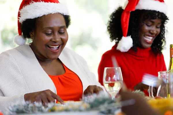 ダイニングルームでの複数世代のアフリカ系アメリカ人の家族は サンタの帽子と笑顔を着て 家族の時間クリスマスのお祝い — ストック写真